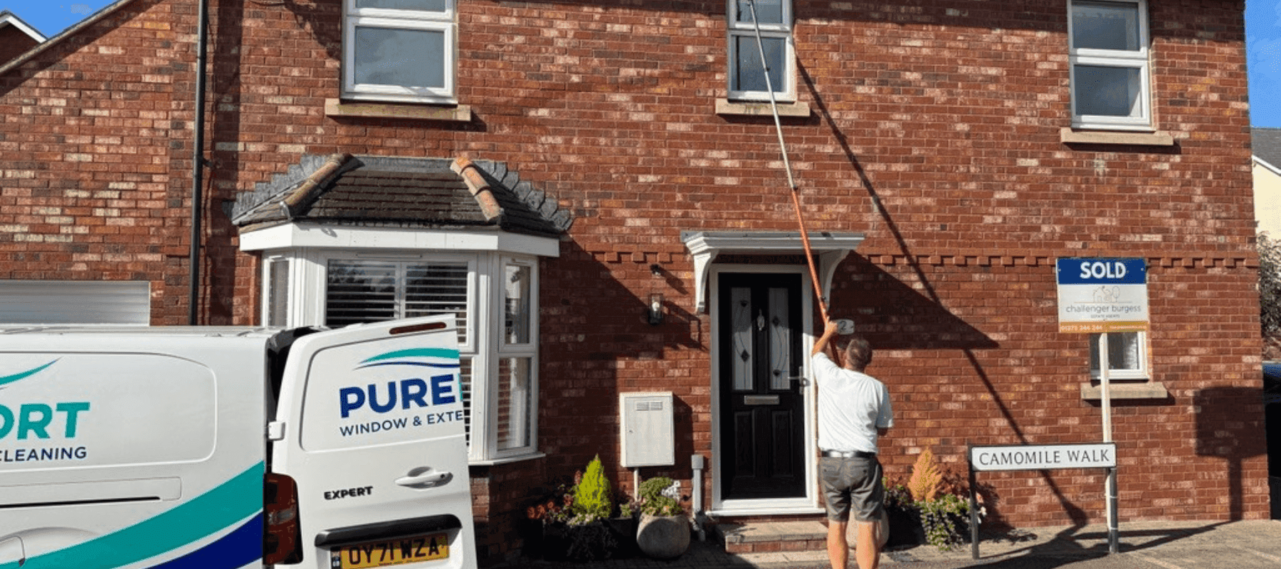 A man cleaning windows on a house with his branded van visible in the left corner.